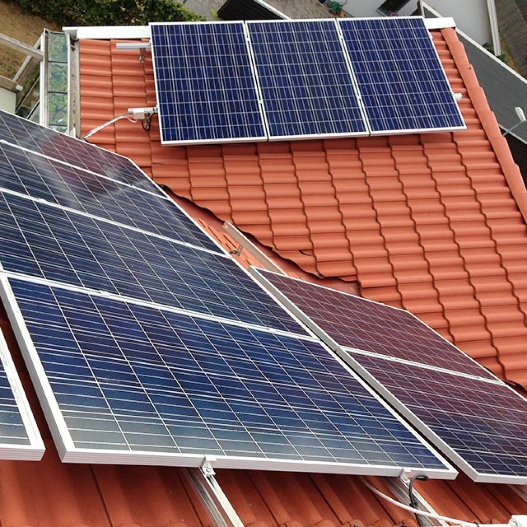 energi_rund Solpaneler installerade på ett tak med röda takpannor, där flera paneler är vinklade för att fånga upp solljuset och generera förnybar energi till byggnaden.